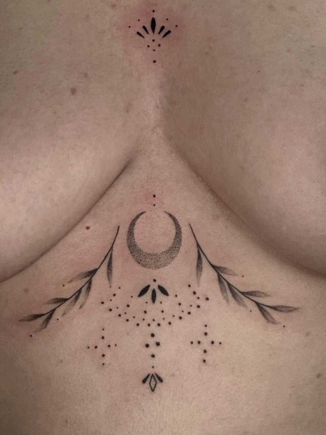 Intricate celestial and botanical under-breast ink